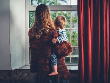 Genç bir wmother küçük yürümeye başlayan çocuk oğlu ile pencereden dışarı bakıyor