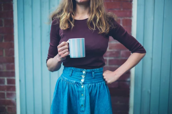 A young woman with a big mug of coffee is standing in the courtyard