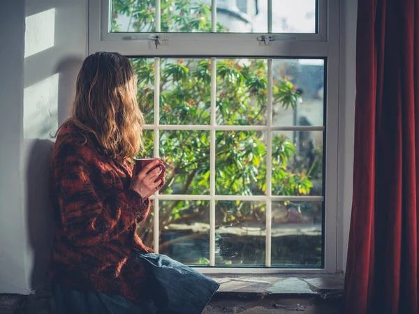 一个年轻的女人坐在窗边喝着一杯茶 — 图库照片