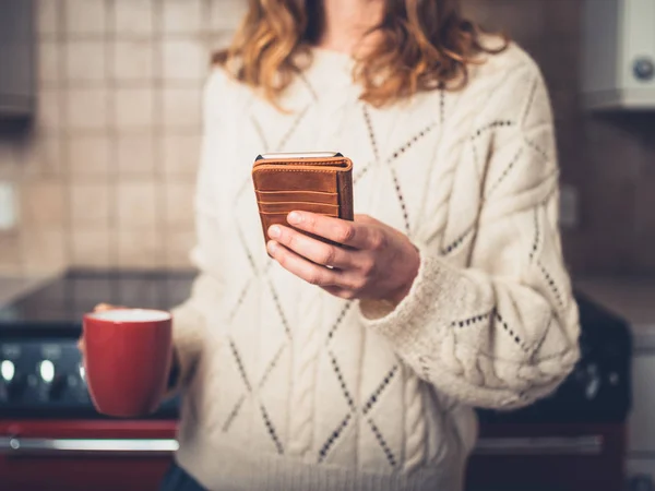 Genç Bir Kadın Bir Fincan Çay Mutfakta Akıllı Telefonunu Kullanarak — Stok fotoğraf