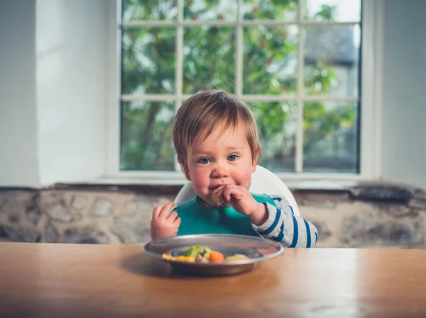 一个可爱的小男孩坐在桌边吃着他的晚餐 — 图库照片