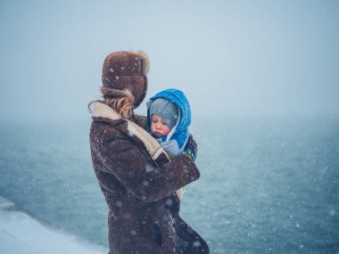 Genç bir anne onu yürümeye başlayan çocuk karda tutan su tarafından duruyor
