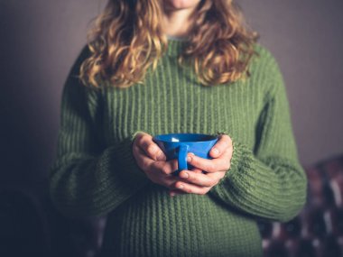 Bir fincan çay ile bir oturma odasında bir jumper giyen genç bir kadın olduğunu