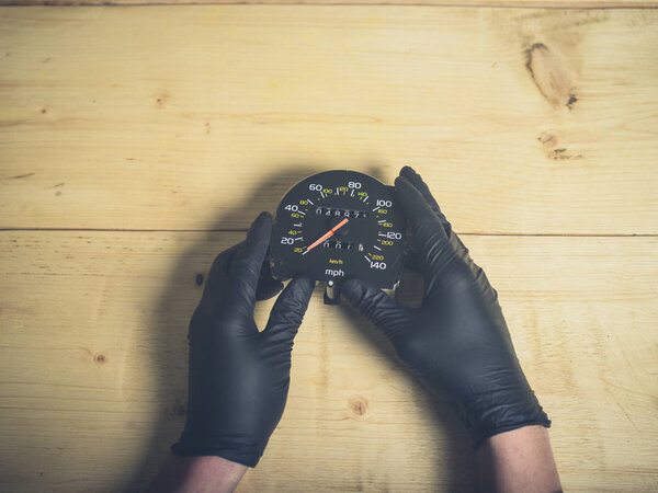 The gloved hands of a man holding a speedometer and odometer at a table