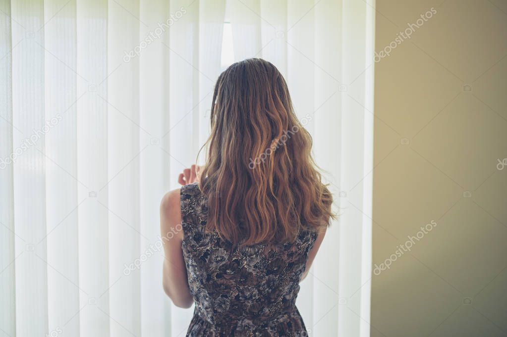 A young woman is peaking through the blinds at home