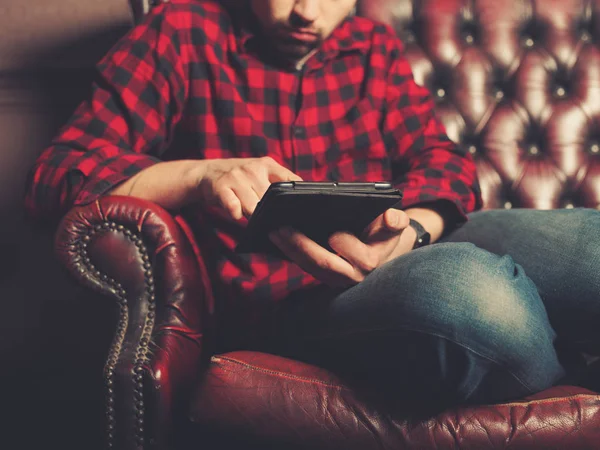 Joven Sentado Sofá Cuero Está Usando Una Tableta — Foto de Stock