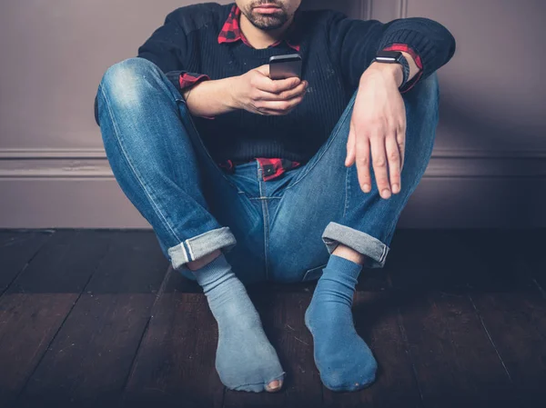 Jovem Desajeitado Está Sentado Chão Madeira Com Seu Telefone Inteligente — Fotografia de Stock