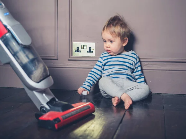 一个可爱的小男孩坐在地板上 并惊讶于吸尘器 — 图库照片