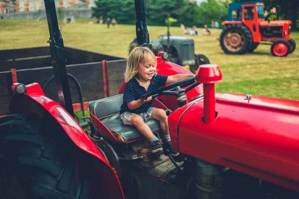 A little toddler is pretending to drive an old tractor
