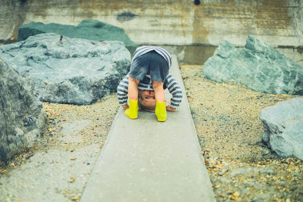 A little toddler is standing on a rocky beach with his head between his legs — Stock Image Little Toddler Standing Rocky Beach His Head His Legs Stock Picture