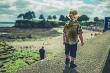 Küçük bir çocuk yazın sahilde bir duvarda yürüyor.