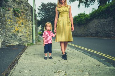 Genç bir anne ve küçük çocuğu yazın bir duvarın yanında yürüyorlar.