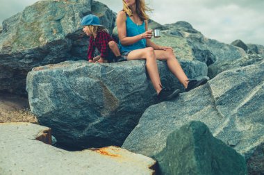 Genç bir anne ve bebeği deniz kenarındaki kayalarda dinleniyorlar.