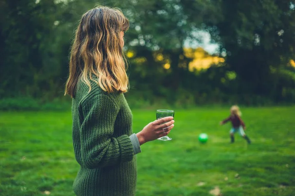 Genç Bir Anne Şarap Içiyor Bebeğinin Gün Batımında Futbol Oynamasını — Stok fotoğraf