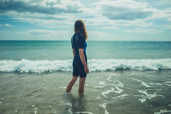 一个穿着湿衣的年轻女子站在海滩上 海浪汹涌而过 — 图库照片