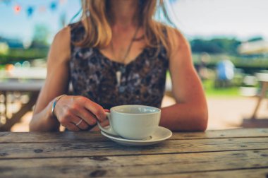 Genç bir kadın yazın açık bir kafede kahve içiyor.