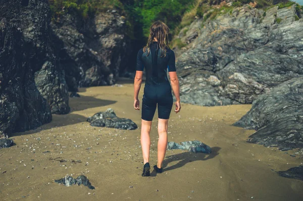 一个穿着湿衣的年轻女子站在沙滩上 上面有一些岩石 — 图库照片