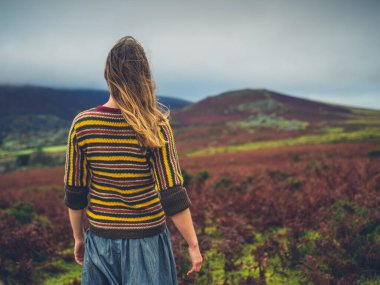 Genç bir kadın sonbaharda kırlarda yürüyor.