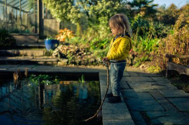 Göletin kenarında sopayla oynayan küçük çocuk.