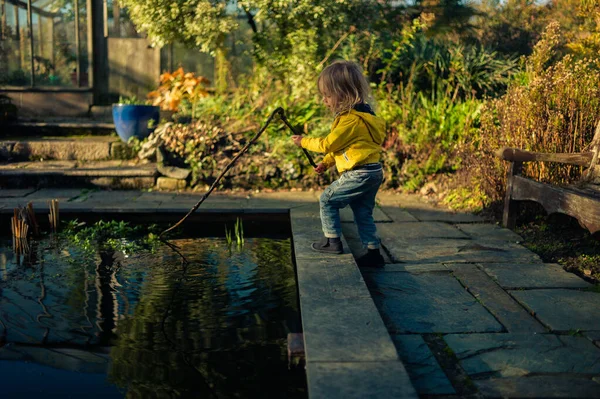 Kleine peuter met een stok die bij een vijver speelt — Stockfoto