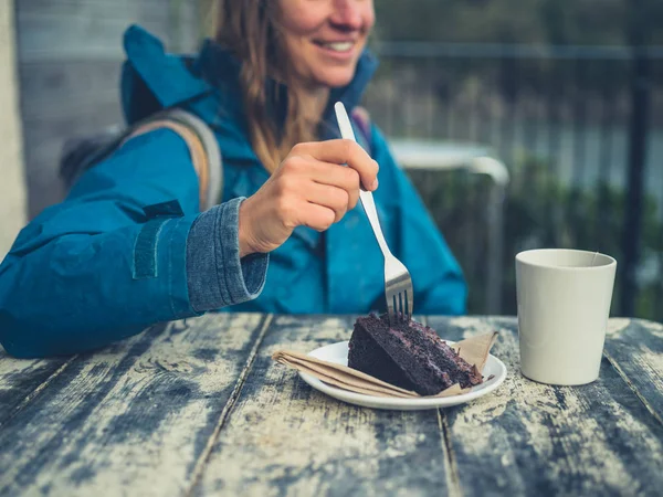 レインコートを着た若い女性が屋外でケーキを食べる — ストック写真