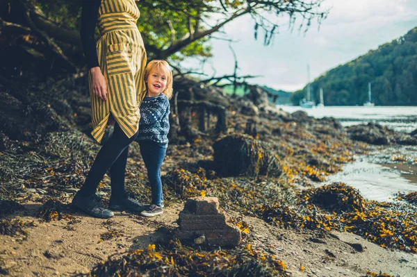 Toddler grabbing his mother's dress by the river in autumn — Stock Photo, Image