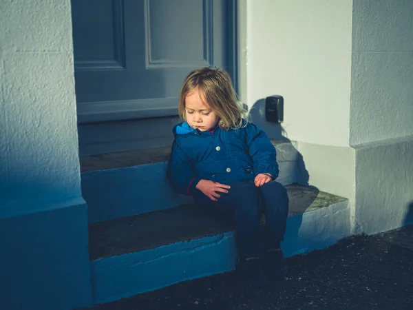 Little toddler sitting on steps outside house in winter — Stok fotoğraf