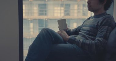 Genç adam kentin penceresinde kahve içiyor.