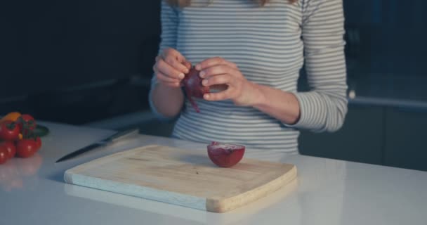 Ung kvinna som skalar lök i köket — Stockvideo