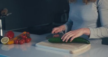 Genç bir kadın mutfakta salatalık kesiyor.