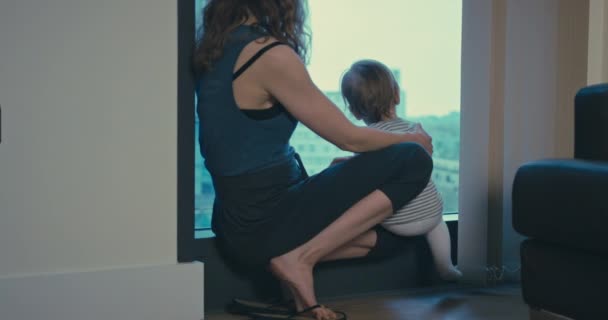 Мать и малыш у окна в городской квартире — стоковое видео