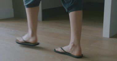 Parmak arası terlik giymiş bir kadın balkona doğru yürüyor.