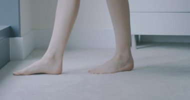 Genç bir kadın yataktan çıkıp pencereye doğru yürüyor.