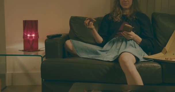 Young Woman Sitting Her Sofa Using Her Smartphone While Eating — Stock Video