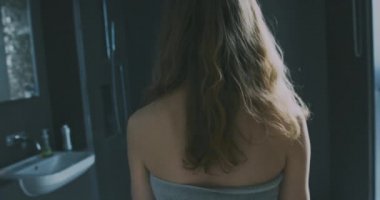 Etrafına havlu sarılmış genç bir kadın bir apartman dairesinde banyoya giriyor. Yavaş çekim el kamerası..