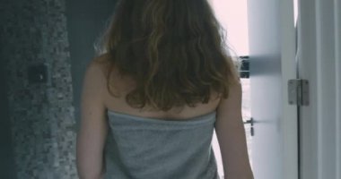 Etrafına havlu sarılmış genç bir kadın sabah bir apartman dairesine giriyor.