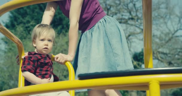 Young Mother Pushing Riding Carousel Her Toddler Boy Playground Handheld — Stock Video