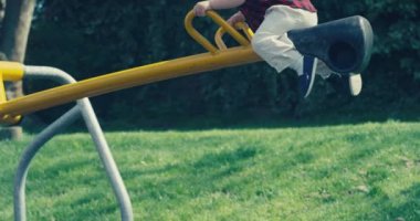 Küçük tatlı bir çocuk yazın parktaki tahterevallide oturuyor.