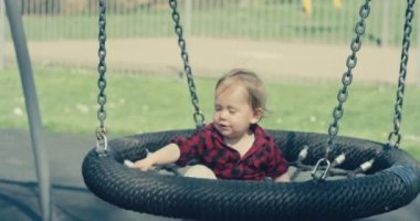 Bir anne, küçük bebeğini çocuk parkında lastik salıncağına itiyor. Ağır çekimde el kamerası.