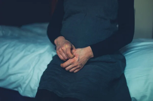 一位患湿疹的孕妇正坐在床上抓着手 — 图库照片