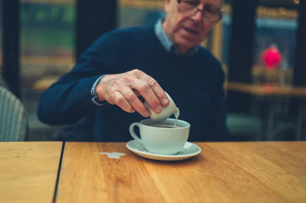 咖啡馆里一个成熟的男人正在往咖啡里倒牛奶 然后把牛奶倒在桌子上 — 图库照片