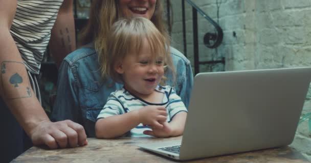 子供が足の上に座っている間にラップトップで自宅で働いている母親のクローズアップ映像 — ストック動画