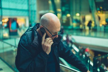 Yetişkin bir adam alışveriş merkezinde telefonla konuşuyor.