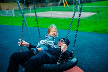 Küçük bir anaokulu öğrencisi büyükbabasıyla parkta örümcek salıncağında oynuyor.