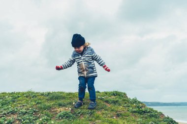 Bir anaokulu öğrencisi kışın sahilde çimenlerde oynuyor.