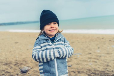 Küçük bir anaokulu çocuğu plajda üşüyor.