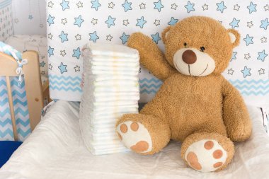 Bebek bezleri, bebek odası ve beşiğinin arka planında oyuncak ayı, bebek bezi kullanma kavramı.