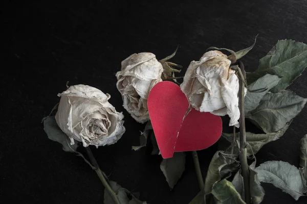 wilted rose flowers and torn in half a paper heart, the concept of a broken heart, breakup, divorce