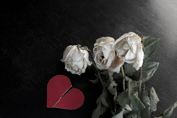 wilted rose flowers and torn in half a paper heart, the concept of a broken heart, breakup, divorce
