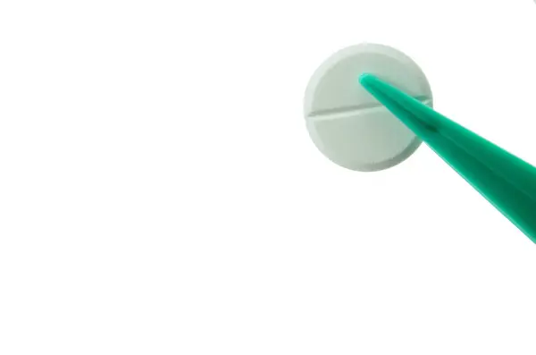 緑色のプラスチック製のピンセットを手に持って白い背景に隔離された白い丸いタブレットを — ストック写真